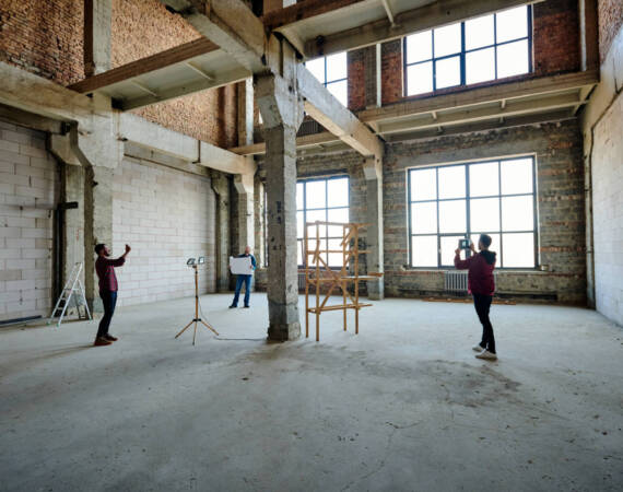 Two young contractors photographing unfinished structure inside building while their colleague looking at sketch on blueprint